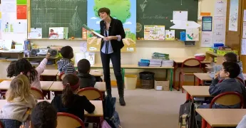 Salle de classe avec une institutrice debout face à ses élèves de dos
