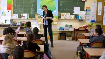 Salle de classe avec une institutrice debout face à ses élèves de dos